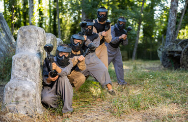 Fototapeta premium Paintball players of one team in camouflages and masks aiming with gun in shootout outdoors