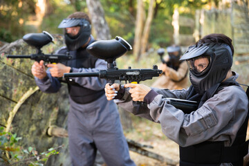 Fototapeta premium Paintball players aiming and shooting with guns at opposing team outdoors