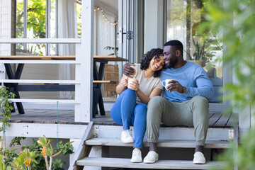 Happy multiracial couple enjoying coffee together on porch, embracing and smiling warmly