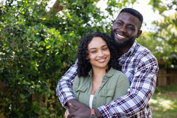 Happy multiracial couple embracing outdoors, smiling warmly in lush green garden