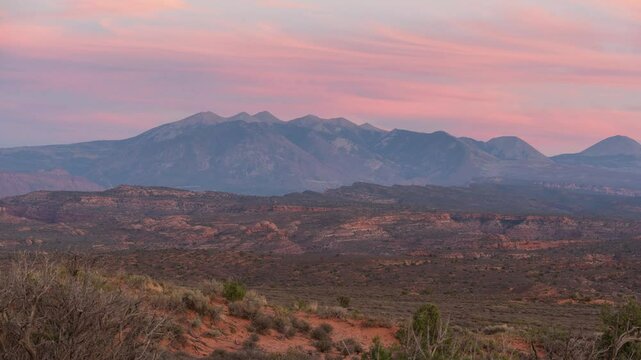 La Sal Mountain range with a beautiful sunset in the background. The mountains are covered in trees and the sky is a mix of pink and orange in Utah