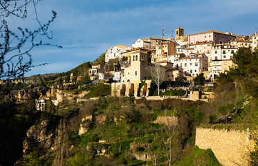 Fototapeta premium Scenic view of Cuenca cityscape on rocky ledge overlooking oldest Catholic parish church of San Miguel on sunny spring day, Spain..