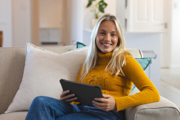 Smiling woman relaxing on couch with tablet at home, enjoying leisure time