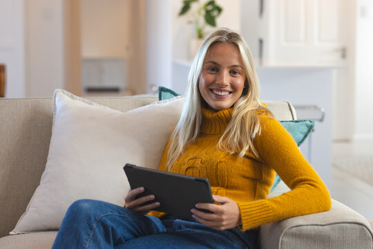 Smiling woman relaxing on couch with tablet at home, enjoying leisure time