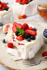 Pavlova cake (meringue dessert) with whipped cream, fresh berries, mint and fig on table, closeup