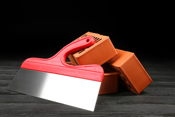 Red bricks and putty knife on wooden table. Building material
