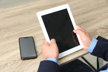 Businessman with tablet and smartphone at wooden table, closeup. Modern technology