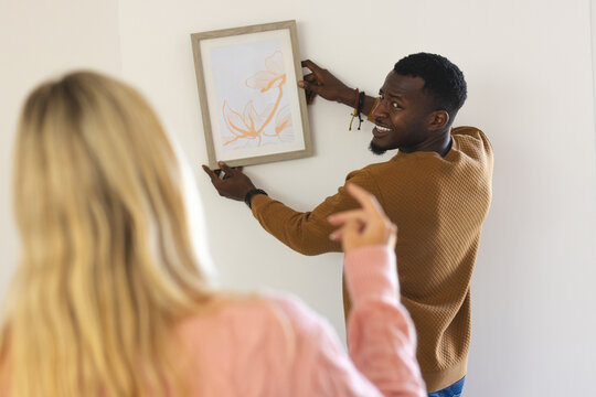 African American man hanging picture while woman gives directions at home