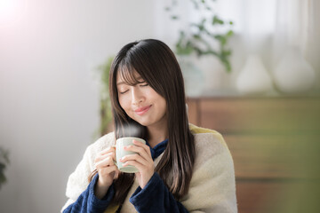 冬のリビングで温かい飲み物を飲むくつろぐ目を閉じる若い女性