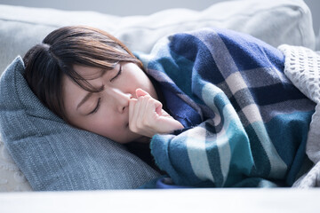 風邪で具合が悪すぎて寝込んでしまう女性のクローズアップ　咳込む