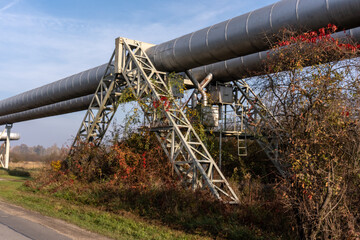 Large industrial pipeline raised on steel support surrounded by fall foliage on sunny day. Concept...