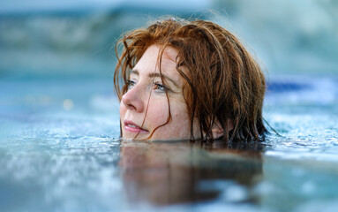 sexy young sensual dreamy redhead woman with wet red hair floats in water, gazing thoughtfully into the distance. The serene atmosphere and soft reflections create a calm, peaceful mood