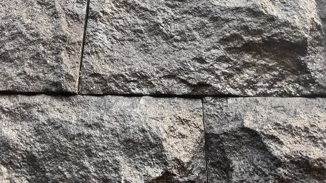 stone wall background. The stone wall is characterised by a textured surface that has been weathered by the passage of time and exposure to the elements.