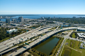 Aerial view of Jacksonville city with high office buildings and american freeway intersection with fast moving cars and trucks. USA transportation infrastructure concept