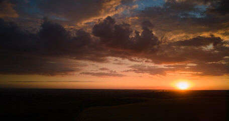 Bright colorful sunset sky with setting sun and vibrant clouds over dark landscape