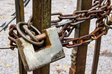 A rusty chain with a lock on it. The lock is silver and the chain is rusted