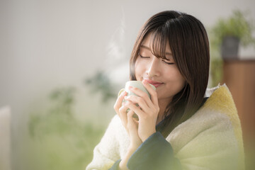 Close-up of a young Japanese (Asian) woman with eyes closed relaxing in a winter living room...