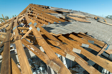 Wind damaged house roof with missing asphalt shingles after hurricane Ian in Florida. Repair of...
