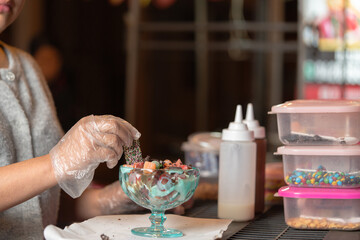 Street vendor preparing colorful dessert with sprinkles and toppings
