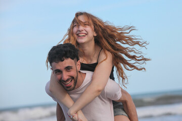 young playful couple having fun on the beach by the ocean on summer day