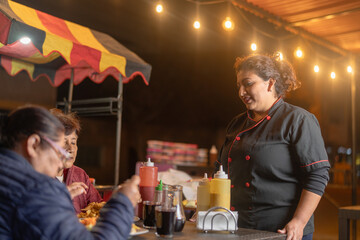 Female chef serving customers eating chicken at night street food stand