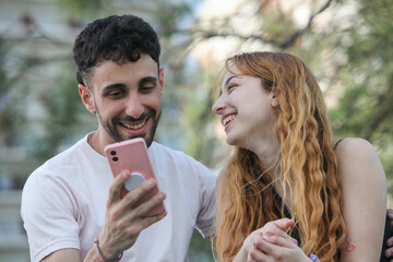 portrait of cheerful young couple using cellphone outdoors 