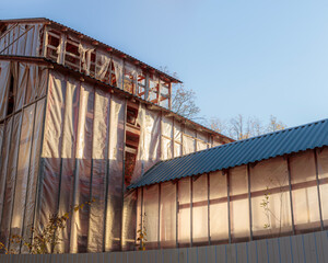 Side view of an old barn structure with exposed beams and partially covered by plastic sheeting.