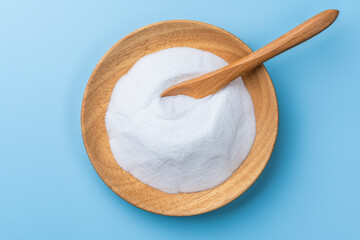 青い背景に重曹の白い粉と木の器と木のスプーンの俯瞰