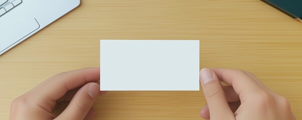 Obraz premium Hands holding a blank business card on a wooden desk.