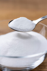 木目テーブルに置かれたガラスの器から重曹の粉をスプーンですくう