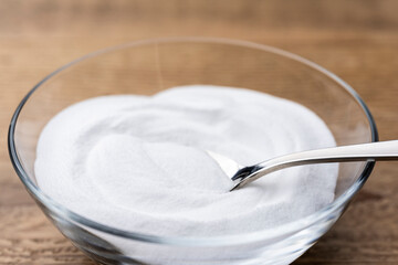 木目テーブルに置かれたガラスの器から重曹の粉をスプーンですくう
