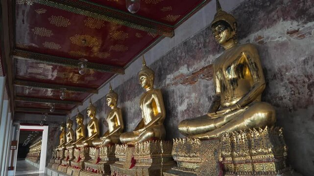 A row of many statues of a gold Buddha sitting in a meditative pose in the courtyard of a Buddhist temple Wat Pho. The most visited tourist place in Bangkok, Thailand