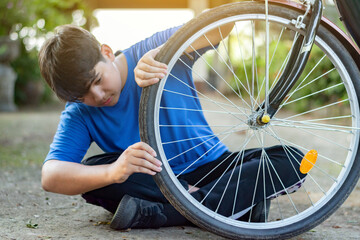 Asian child in blue t-shirt holding front tire or wheel and checking it before riding in front of...