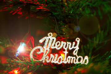 Close up "Merry Christmas" label make from metal on decorated green Christmas tree branch