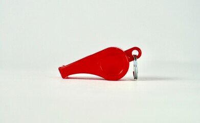 One red whistle with no string isolated on plain horizontal background from side angle view.