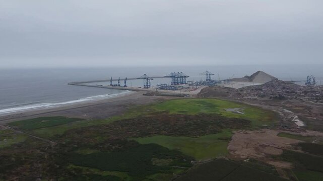 Aerial shot of a construction site of megaport being built in Peru in the city of Chancay. Drone flies above wetlands towards the port. Big blue cranes can be seen in the distance.