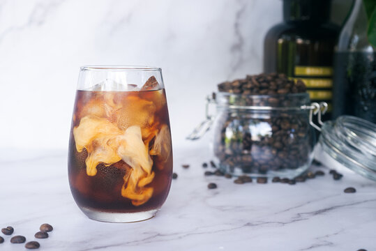 a glass of homemade iced cold brew coffee with milk on white marble table.