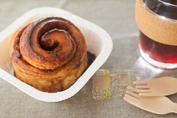take away cinnamon bun in paper cup with glass reusable coffee cup.
