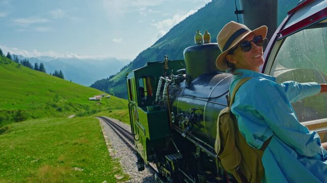 A girl tourist in a hat and glasses looks at the alpine meadows smiling and delighted by the journey from the tourist red rotary train going from the city of Brienz above Lake Interlaken, Switzerland