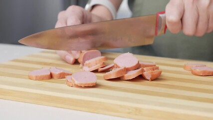Close-up of a woman cutting sausage on a wooden cutting board in a kitchen setting with different ingredients.