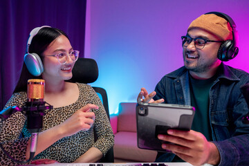 Young asian man and woman host streaming podcast with condenser microphone work on tablet at home...