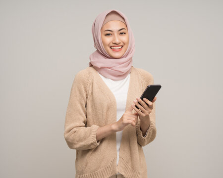 Portrait happy young asian muslim woman holding smartphone standing on isolated white background. Beautiful Attractive Muslim woman wearing abaya and hijab fashion costume shot in studio
