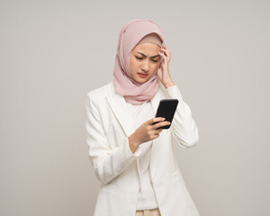 Unhappy young asian business muslim woman holding smartphone standing on isolated white background. Feeling stressed business Muslim woman wearing abaya and hijab fashion costume shot in studio