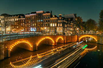 Amsterdam’s historic canal bridges illuminated at night. The Keizersgracht and Reguliersgracht intersection glows romantically, reflecting typical Dutch architecture and city lights in the water.