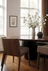 Fototapeta premium A cozy dining room with a wooden table and chairs, a vase of white flowers, and a framed artwork on the wall.