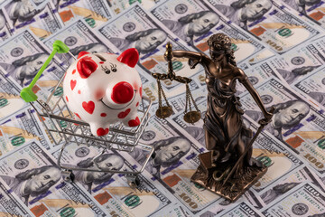 Fototapeta premium Themis figure and a piggy bank against the background of 100 US dollar bills