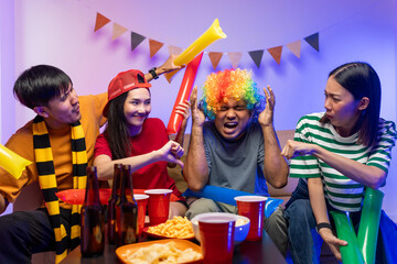 Fototapeta premium Sports fans feel sad when the team they support loses. Group of asian friends man and woman watching cheering football match on TV at home. Eating snack and drinking beer.