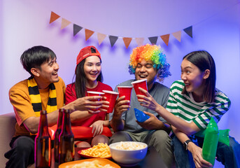 Group of asian friends man and woman watching cheering football match on TV at home. Eating snack...
