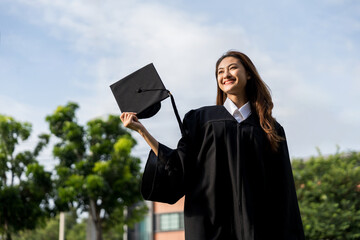 Happy asian woman in graduation costume with cap standing outdoor public park. College degree...