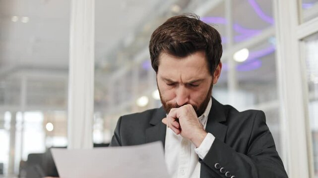 Concerned businessman in a suit reviews paperwork with a worried expression. Man thinks hard while reading a document in office. Bad negative news work result rejection letter feeling disappointed.